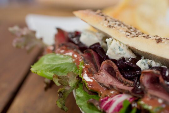 Close-up of a vibrant, artisan Italian panini filled with blue cheese, caramelized onions, roast beef, and mixed Italian lettuce, showcasing a rich, flavorful bite.