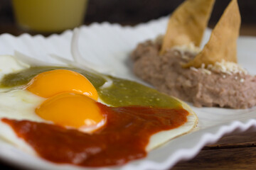 Close-up of classic huevos rancheros with chipotle and serrano pepper sauce, black beans, and crispy tortilla chips, elegantly plated Mexican breakfast.