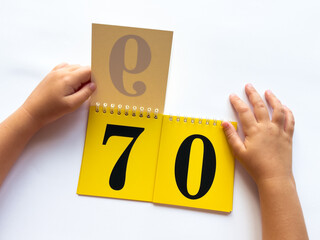 Childs hands flip through yellow pages with numbers. Displaying number 70 on white background
