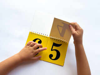 A child turns a page of learning numbers to the next number on a bright yellow background