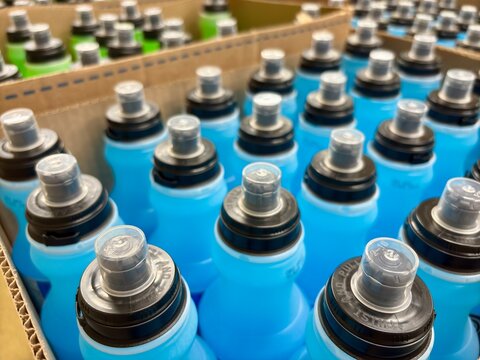 Rows of blue sports drink bottles with black caps in cardboard packagi