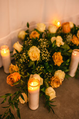 Candles and beige roses arranged with greenery on a soft-lit surface