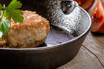 Cast iron frying pan with fried cutlet and tomatoes on wooden table,close up