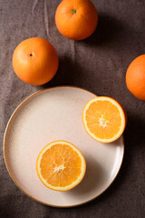 Fresh navel oranges on brown ceramic plate on brown fabric background. Top view.
