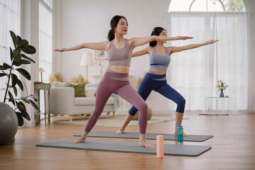 Obraz premium Two Asian woman wearing sportwear practicing yoga at home studio. Couple females exercising with yoga for flexibility body in living room. Health care and wellness activities.