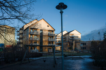 Residential area in Scandinavia, Wooden multi-storey residential buildings illuminated by low winter sun against blue sky, deep shadow on playground with street lamp in foreground, V&auml;ster&aring;s, Sweden