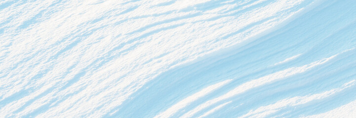 Wide panoramic winter background with snowy ground. Natural snow texture. Wind sculpted patterns on snow surface.