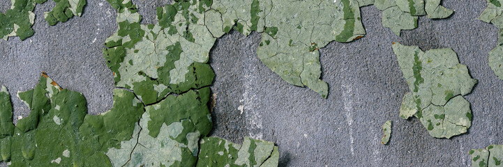 Peeling paint on the wall. Panorama of a concrete wall with old cracked flaking paint. Weathered rough painted surface with patterns of cracks and peeling. Panoramic texture for background and design.