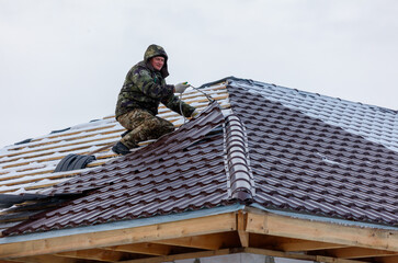 A man is working on a roof, wearing a green jacket