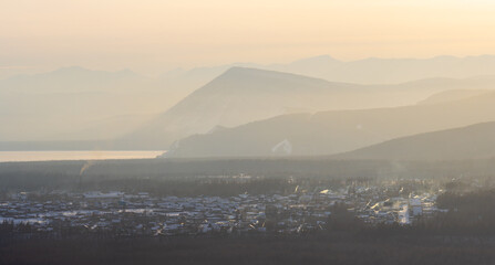 Beautiful winter landscape. View of a large Siberian village in a mountain valley. Houses surrounded by forest. In the distance is the shore of Lake Baikal and the mountains. Buryatia, Siberia, Russia
