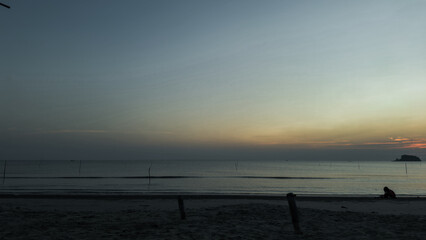 Obraz premium Serene Sunset Over the Sea: A solitary figure silhouetted against the breathtaking panorama of a sunset over the ocean. The calming hues of twilight cast a peaceful glow on the sandy shore.