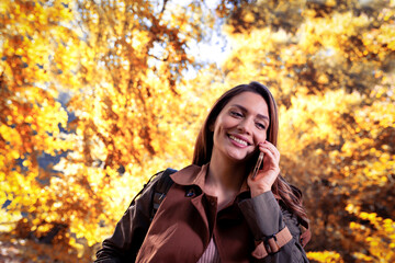 Happy young woman using her phone in autumn park