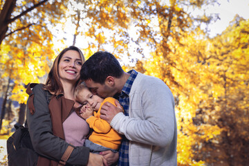 Fototapeta premium Young family with little son in autumn park on sunny day. Family autumn portrait