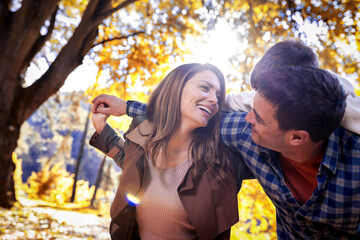 Smiling father gives his young son a piggyback ride on his back in autumn park. Mother is smiling....