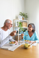 Mature married couple enjoying pasta salad for lunch. Couple looking at each other smiling while eating.