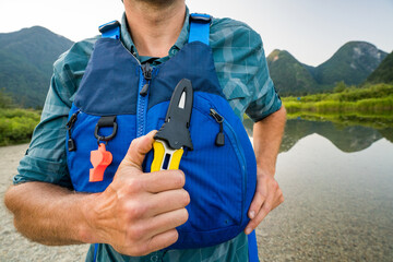 Paddler holds knife in sheath on the front of a PFD, lifejacket.