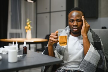 African American man sick with flu or cold at home. He takes medicine and drinks tea