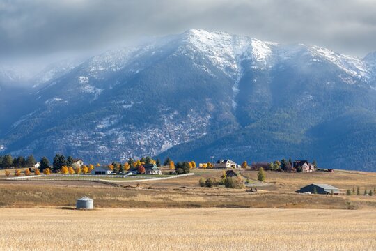 Autumnal countryside scene with snow-capped mountains. Homesteads and a grain silo are nestled in the valley. , Kalispell, Montana, USA
