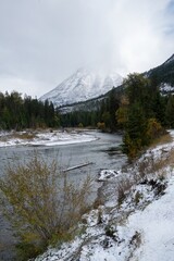 Snowy mountain river scene. A tranquil river winds through a wintry forest, with snow-capped peaks in the background.  Glacier National Park, West Glacier, Montana, USA