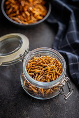 Dried salted worms. Roasted mealworms in jar on black table.
