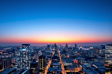 Obraz premium A vibrant city skyline at sunset with illuminated buildings, gradient sky transitioning from orange to blue, and a bustling urban atmosphere. Ai generative