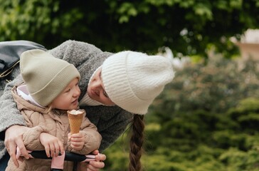 Mother supports her daughter while she learns to ride a scooter outdoors, close-up. The concept of...