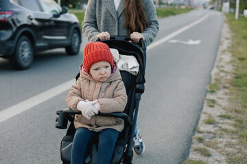 Close up of young mother in warm coat pushing baby stroller and slowly crossing street on...