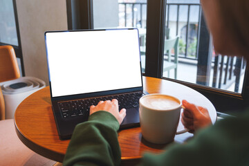 Mockup image of a woman typing on laptop computer with blank white desktop screen while drinking coffee in cafe