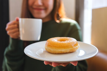 Closeup of a young woman holding and drinking hot coffee and eating donut in cafe