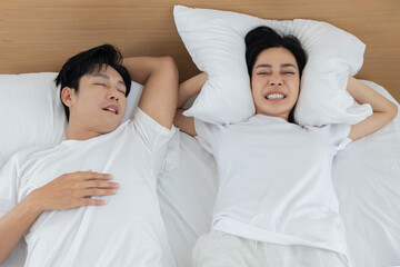 Portrait of asian man snoring while a woman blocking her ears pillow