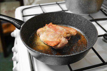 Juicy turkey meat sizzles in a black skillet placed on a gas stove in a kitchen