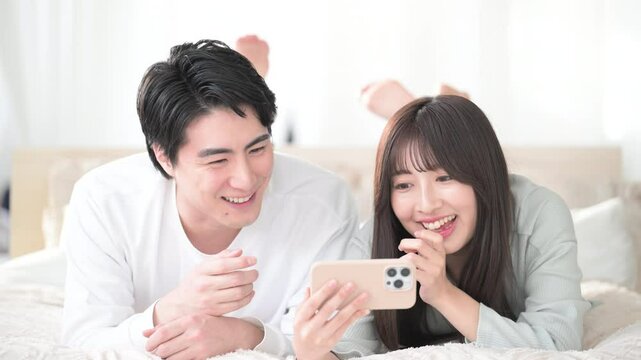 Close-up video of a couple in bed with their phones, watching a video and smiling.