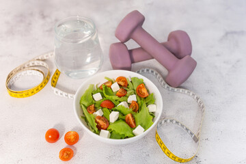 Healthy lifestyle concept with salad bowl, water, dumbbells and measuring tape. Diet concept.