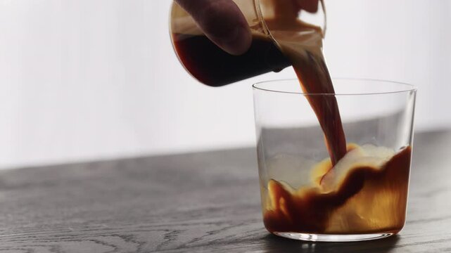 Slow motion pour espresso in tumbler glass on black aok table