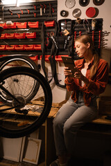 Technology in bicycle repair. Woman mechanic or repairman using a digital tablet in a bicycle repair shop.