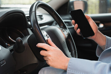 Close-ups of woman's hands holding the steering wheel and using cell phone, the concept of safe driving