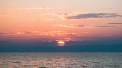 Fototapeta premium Beautiful sunset sky with scattered light clouds in shades of orange, pink, and blue over the horizon