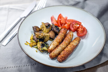 Small roasted sausages with herb mushrooms and fresh tomatoes on a gray plate, barbeque party snack or lunch meal, selected focus