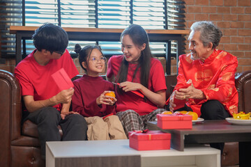 happy asian family gathering at home to celebrate Chinese New Year,sitting on couch,talking,giving red envelope and eating