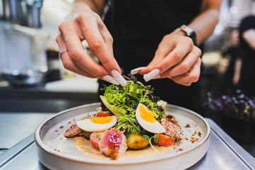 A chef delicately garnishes a vibrant salad with fresh greens, sliced eggs, and colorful ingredients, showcasing culinary creativity and attention to detail in a professional kitchen setting.