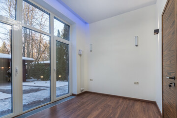 A spacious empty room with a panoramic window in a country house. Unfurnished. .From the window there is a view of the courtyard on a sunny winter day.