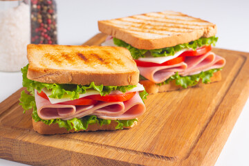 Close-up of two sandwiches with bacon, salami, prosciutto and fresh vegetables on rustic wooden cutting board. Club sandwich concept