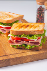 Close-up of two sandwiches with bacon, salami, prosciutto and fresh vegetables on rustic wooden cutting board. Club sandwich concept