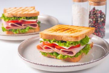 Close-up of two sandwiches with bacon, salami, prosciutto and fresh vegetables on rustic wooden cutting board. Club sandwich concept