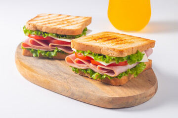 Close-up of two sandwiches with bacon, salami, prosciutto and fresh vegetables on rustic wooden cutting board. Club sandwich concept