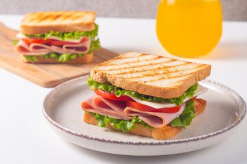 Close-up of two sandwiches with bacon, salami, prosciutto and fresh vegetables on rustic wooden cutting board. Club sandwich concept