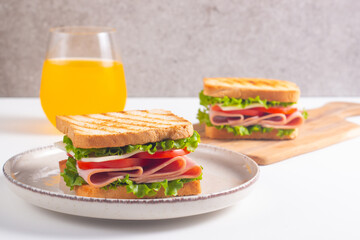 Close-up of two sandwiches with bacon, salami, prosciutto and fresh vegetables on rustic wooden cutting board. Club sandwich concept
