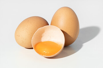 Studio shot of Two whole brown eggs and a broken eggshell containing an egg yolk isolated on white...