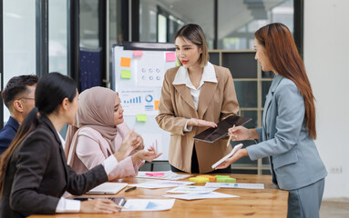Group of asian professionals collaborating and working together in a  office. They are discussing project solutions and working on paperwork. The team looks happy, successful.
