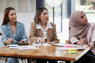 Group of asian professionals collaborating and working together in a  office. They are discussing project solutions and working on paperwork. The team looks happy, successful.

